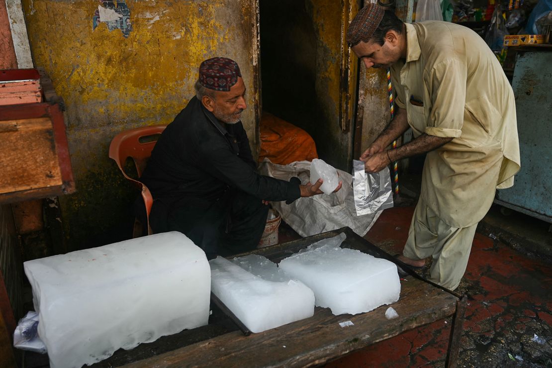 A vendor selling ice, slices a piece from an ice block for a customer at his shop on a hot summer noon in in Karachi on May 27, 2024.