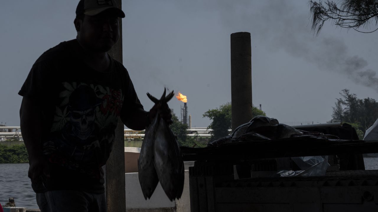 A fisherman prepares fish from the catch of the day in front of chimneys of the Olmeca oil refinery belonging to the company Petroleos Mexicanos (PEMEX), which along with six others is part of the National Refining System (SNR) located in Paraiso, Tabasco state, Mexico on May 20, 2024. While the north of Mexico is home to industrial hubs closely linked to the neighboring United States, the world's largest economy, the south has historically lagged behind economically, prompting Mexico's outgoing President Andres Manuel Lopez Obrador to pursue economic development projects for the region. (Photo by Yuri CORTEZ / AFP) (Photo by YURI CORTEZ/AFP via Getty Images)