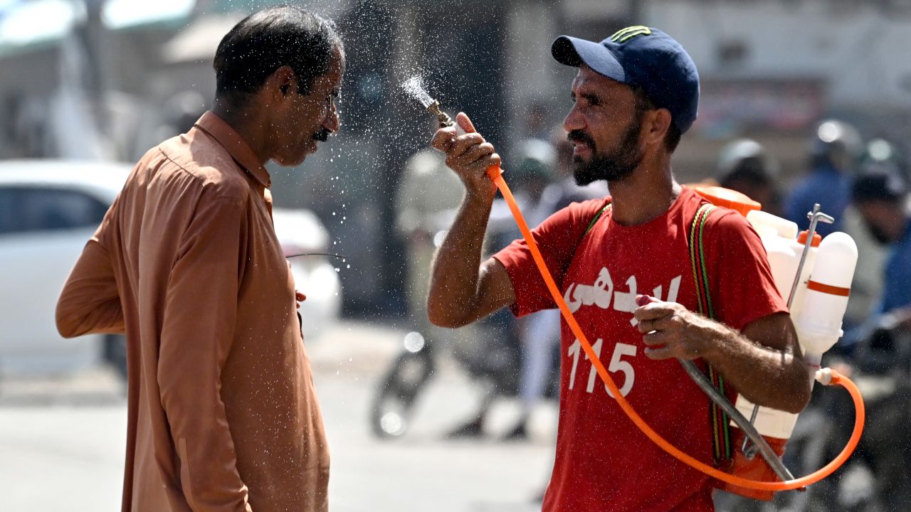 A volunteer sprays water on a bypasser's face along a street during a hot summer day in Karachi on May 30, 2024, amid the ongoing heatwave. (Photo by Asif HASSAN / AFP) (Photo by ASIF HASSAN/AFP via Getty Images)