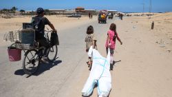 TOPSHOT - Palestinian children use a hazmat suit to transport belongings as they flee the area of Tel al-Sultan in Rafah in the southern Gaza Strip on May 30, 2024, amid the ongoing conflict between Israel and the militant group Hamas. (Photo by Eyad BABA / AFP) (Photo by EYAD BABA/AFP via Getty Images)