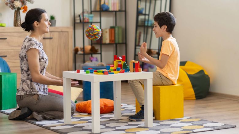 A young boy engages in building block activities during a therapy session, which can be used to depict motor skills development, with a psychologist overseeing the engagement