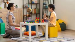 A young boy engages in building block activities during a therapy session, which can be used to depict motor skills development, with a psychologist overseeing the engagement