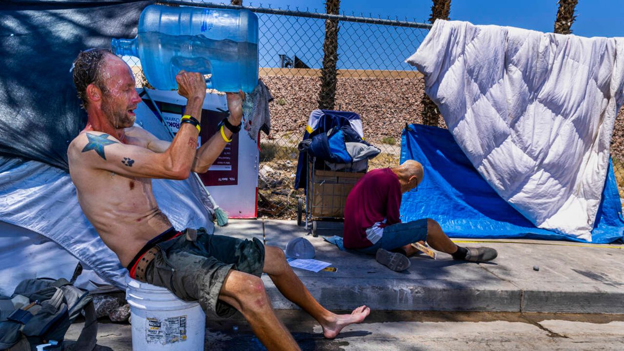 Milton John Scott III, who is unhoused, pours a jug of water on his head to escape the heat and wash up at his shelter in Las Vegas, Nevada on June 5, 2024.
