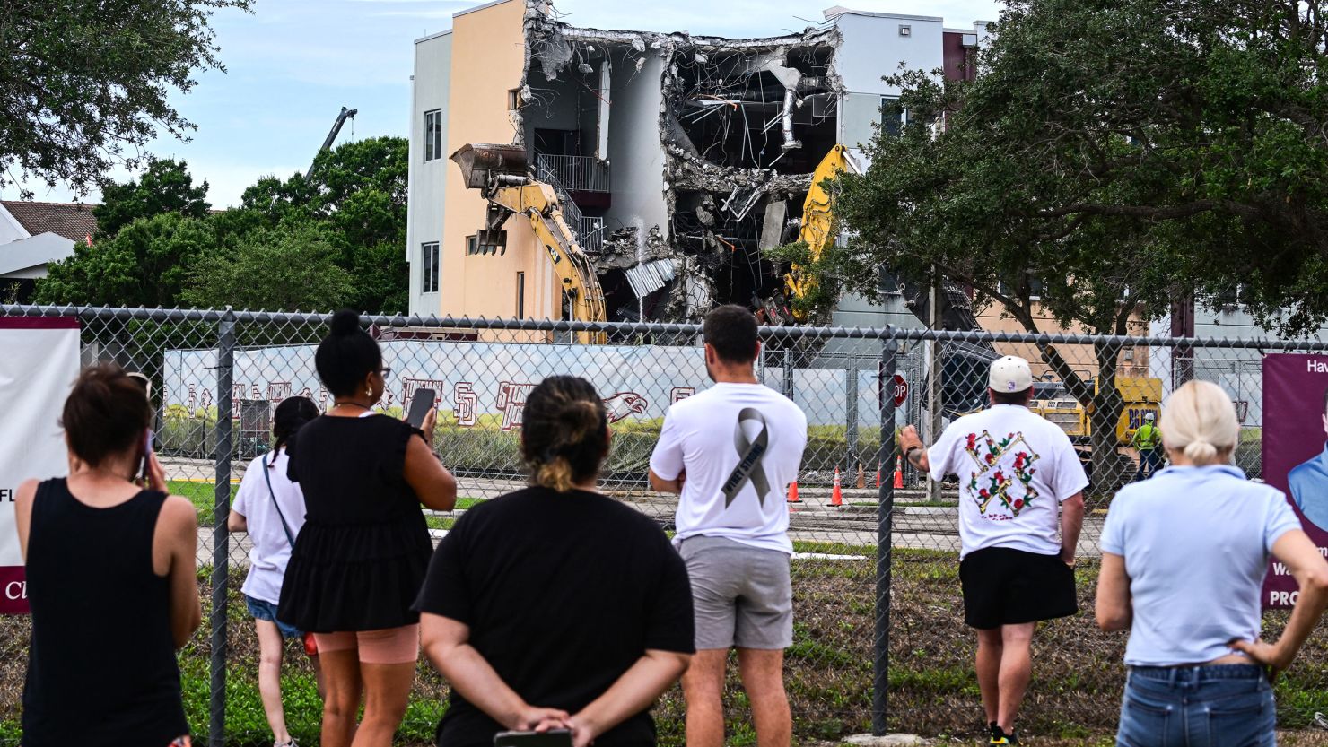 Onlookers watch as crews start demolition of the Marjory Stoneman Douglas High School 1200 building on Friday.