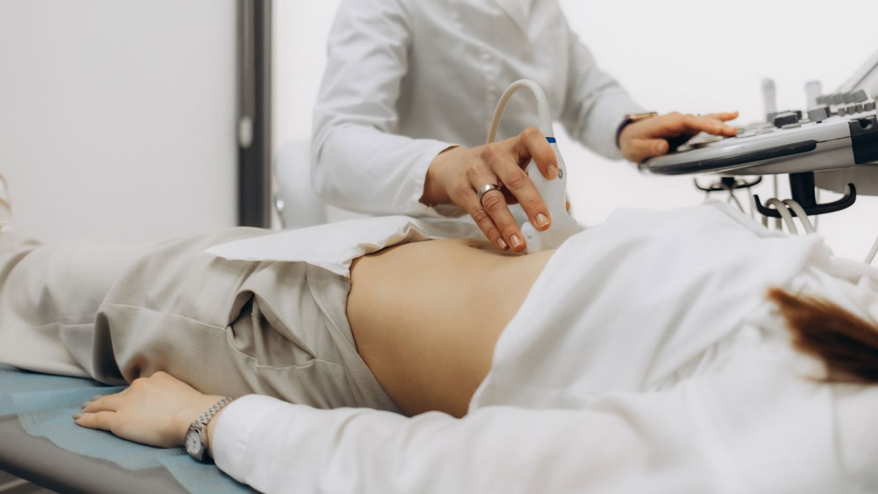 Closeup of male doctor moving ultrasound probe on pregnant woman's stomach in hospital