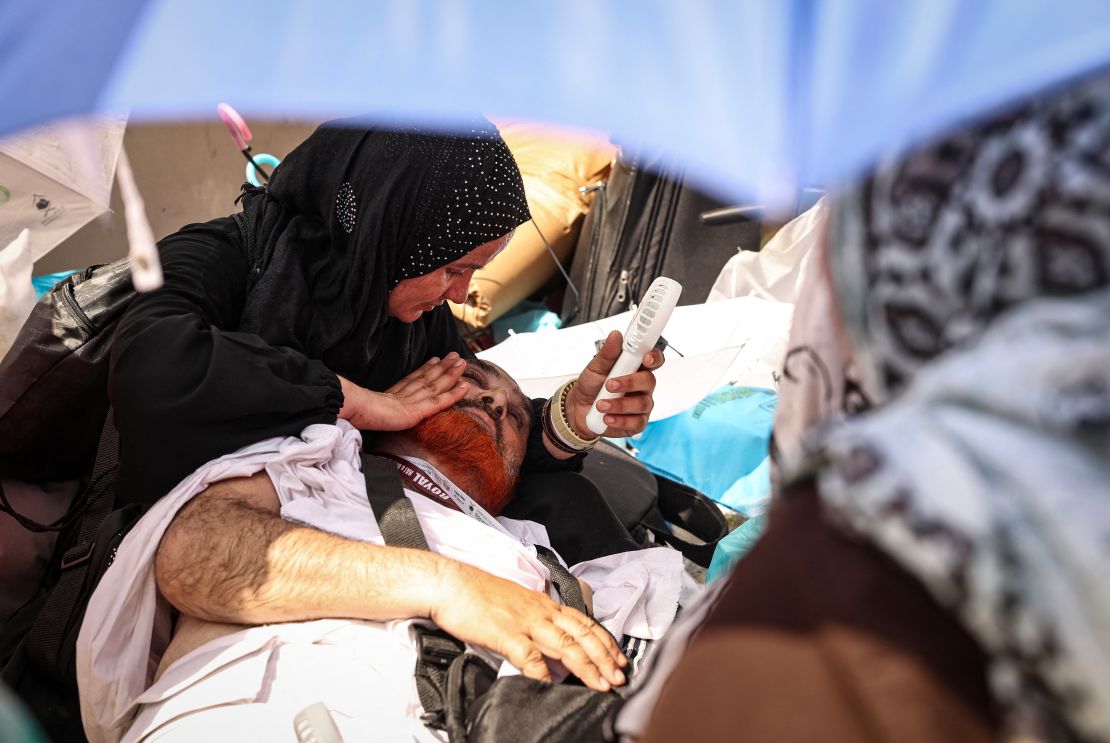 Una donna usa un ventilatore per rinfrescare un uomo disteso a terra durante l'Hajj.