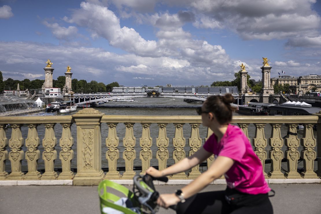 A cyclist rides looking at Alexandre III bridge where rows of seats are set up for the games's opening ceremony.