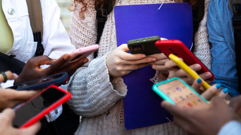 Close up of young college students hands holding mobile phones. Teenagers addicted to smartphones and technology. Group of friends sharing content on social media. Technology concept.