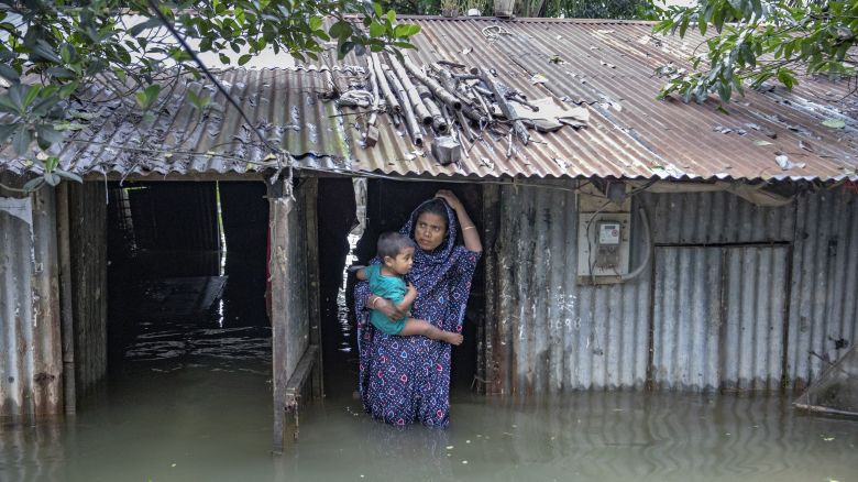 SYLHET, BANGLADESH - JUNE 20: A mother holds her son in front of her house on flood water on June 20, 2024 in Sylhet, Bangladesh. Heavy monsoon rains have unleashed landslides and floods that displaced millions more across northern Bangladesh and India. Deadly landslides and flooding are common across South Asia during the summer monsoon season that stretches from July to September. (Photo by Salahuddin Paulash/Drik/Getty Images)