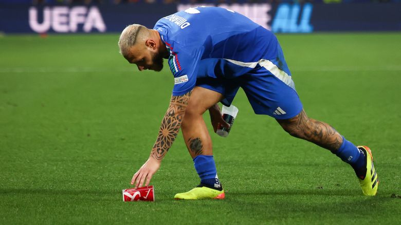 Federico Dimarco collects beer cups from the pitch which fans have thrown.