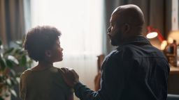 Back view portrait of caring single father comforting young son sitting on bed together against window light