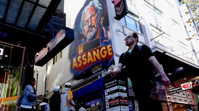 People walk past a mural of Wikileaks founder Julian Assange on George Street in the central business district of Sydney on June 25, 2024. Julian Assange was released from prison on June 24 and has left Britain, WikiLeaks said, as he reached a landmark plea deal with US authorities that brought an end to his years-long legal drama. (Photo by Saeed KHAN / AFP) (Photo by SAEED KHAN/AFP via Getty Images)