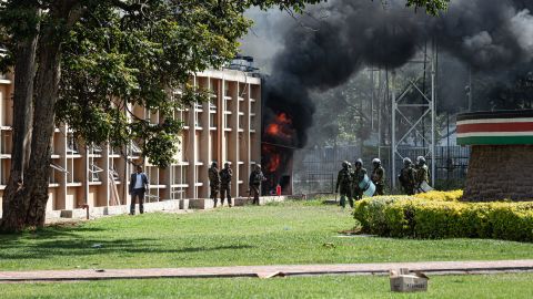 NAIROBI, KENYA - JUNE 25: Kenyan police officers stand as fire comes out of the parliament building during a protest against the finance bill on June 25, 2024 in Nairobi, Kenya. Last week saw several days of protests, mainly by young Kenyans, against a proposed finance bill that promises to raise taxes on a variety of goods. The outcry spurred the government to withdraw several contentious provisions, including taxes on bread and vehicles, but the bill ed a second-round vote and a parliamentary committee is now considering amendments. (Photo by Patrick Meinhardt/Getty Images)