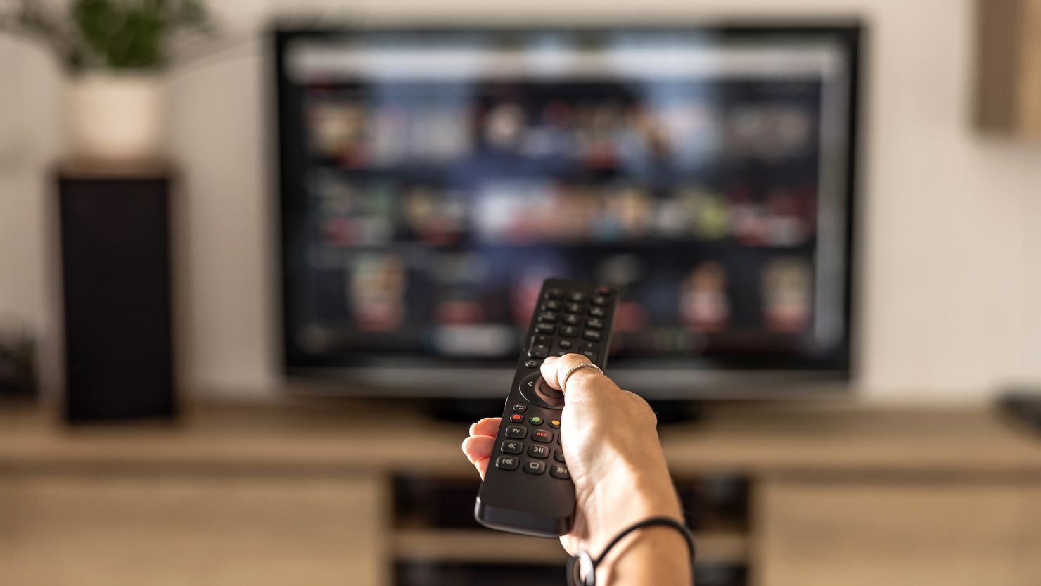 Close up of a person holding a control remote with a television screen on the background.