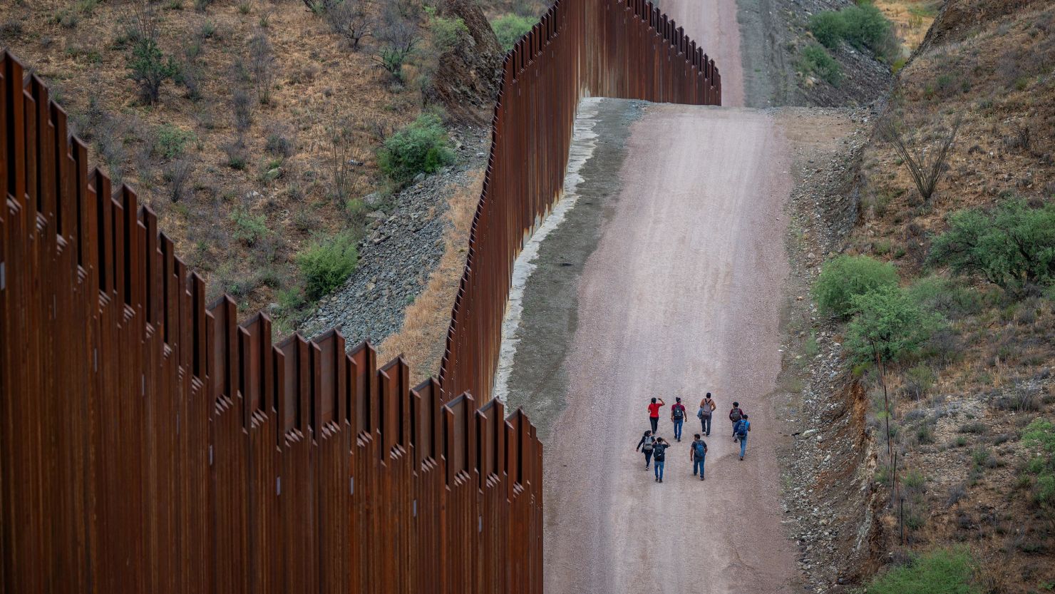 Migrants seeking asylum from Central and South America walk alongside border fencing after illegally crossing over into the US on June 24, 2024, in Ruby, Arizona.