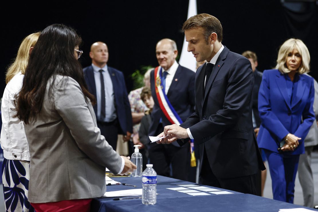 Emmanuel Macron, vergezeld door zijn vrouw Brigitte Macron (rechts), houdt het stembiljet vast om te stemmen in de tweede ronde in een stembureau in Le Touquet, Noord-Frankrijk.