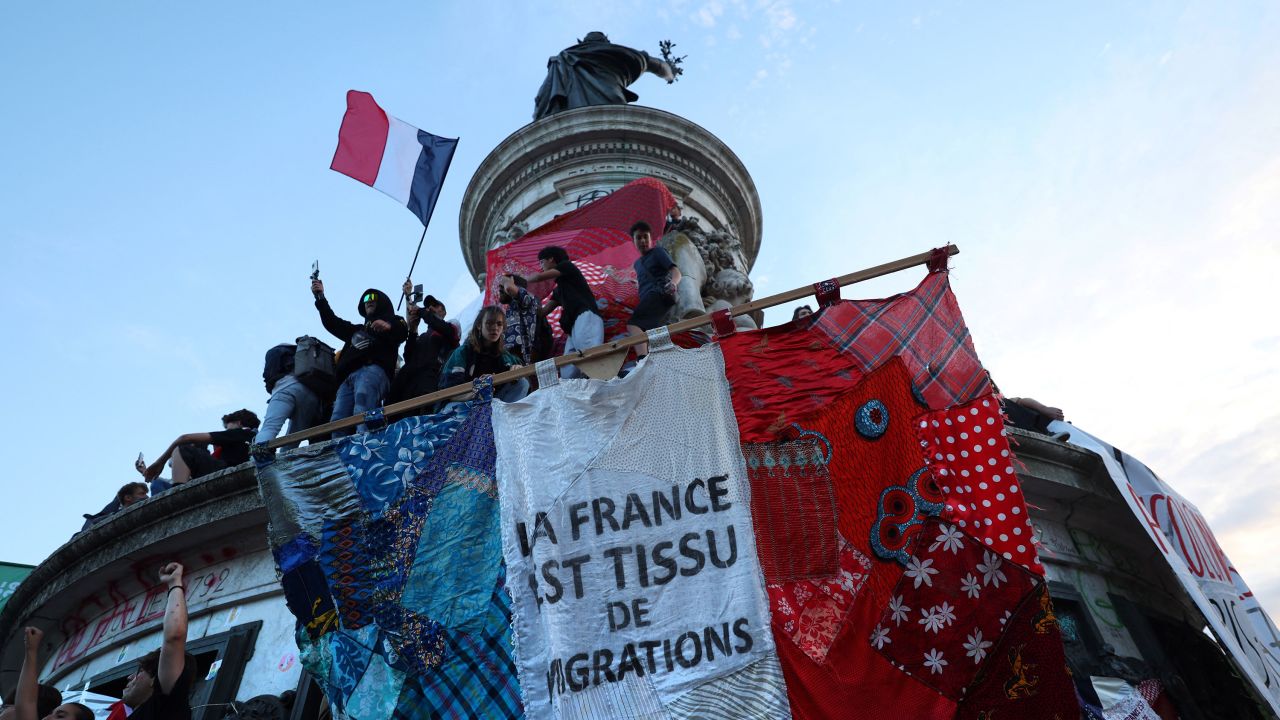 People stand with a giant banner that reads "France is the fabric of migration" during an election night rally at Place de la Republique in Paris on July 7.