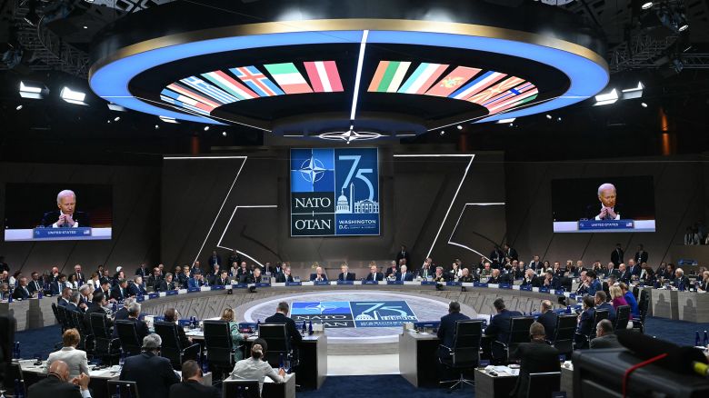 A scene setting picture of dignitaries gathered around a large round table. A sign on the opposing wall marks it as NATO 75.