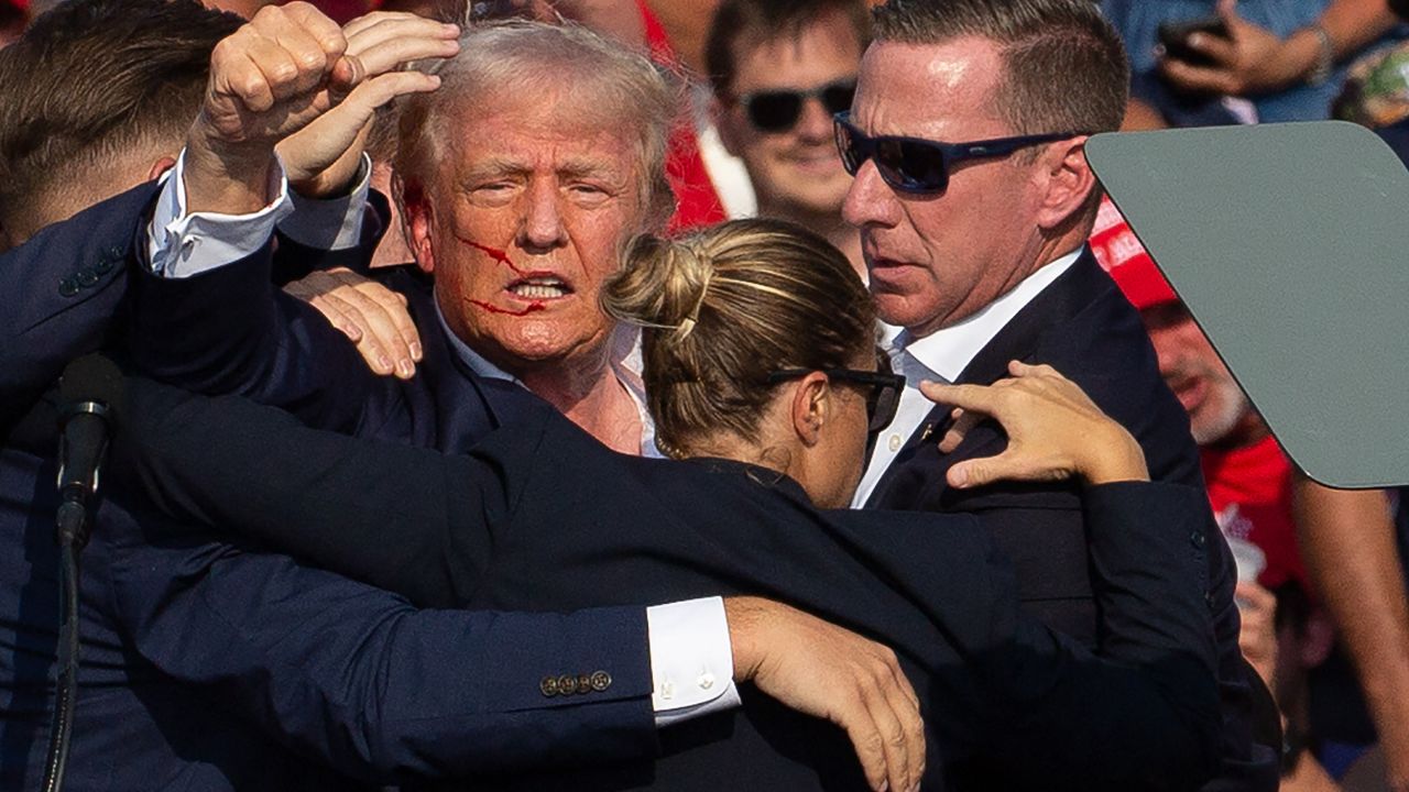 US Republican candidate Donald Trump is seen with blood on his face surrounded by secret service agents as he is taken off the stage at a campaign event at Butler Farm Show Inc. in Butler, Pennsylvania, on July 13, 2024. Trump was hit in the ear in an apparent assassination attempt by a gunman at a campaign rally on Saturday, in a chaotic and shocking incident that will fuel fears of instability ahead of the 2024 US presidential election. The 78-year-old former president was rushed off stage with blood smeared across his face after the shooting in Butler, Pennsylvania, while the gunman and a bystander were killed and two spectators critically injured. (Photo by Rebecca DROKE / AFP) / QUALITY REPEAT (Photo by REBECCA DROKE/AFP via Getty Images)