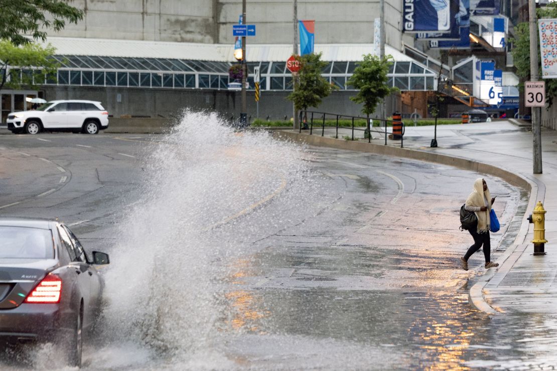 TORONTO, ONTARIO - 16 LUGLIO - Un pedone evita di bagnarsi da un'auto di passaggio su Race Street nel centro di Toronto, 16 luglio 2024. Environment Canada ha emesso un avviso di pioggia e un forte avviso di temporale per Toronto e l'area metropolitana di Toronto fino al primo martedì pomeriggio.  L'allerta prevede pioggia fino a 75 mm con rovesci durante tutta la giornata, a tratti anche forti.  Andrew Francis Wallace/Toronto Star (Andrew Francis Wallace/Toronto Star tramite Getty Images)