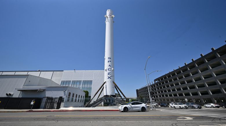 A driver in a Tesla drives past the Falcon 9 Booster at SpaceX Headquarters in Hawthorne, California on July 16, 2024. Elon Musk on July 16 said he will move the headquarters of SpaceX and X to Texas after a California law blocked schools from forcing teachers to notify parents about changes to a student's gender identity. (Photo by Frederic J. BROWN / AFP) (Photo by FREDERIC J. BROWN/AFP via Getty Images)