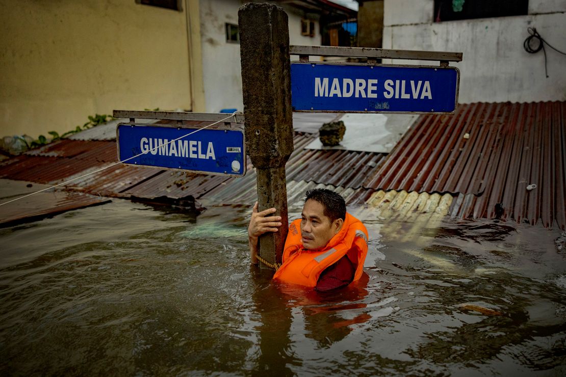 A resident holds on to a street sign in a road flooded by Typhoon Gaemi and monsoon rains on July 24, 2024 in Quezon City.