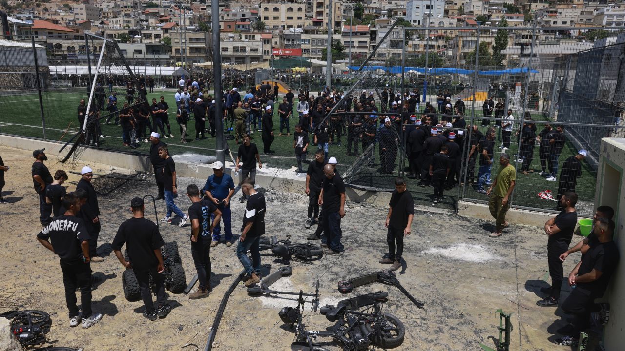 Members of the Druze community look at the damaged fence and scattered objects at a football pitch, a day after 12 people were killed there in a rocket strike from Lebanon, in the Druze town of Majdal Shams in the Israel-annexed Golan Heights, on July 28, 2024.