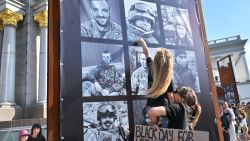 A mother holds her daughter who points the portrait of her late father at an exhibition in the sidelines of a memorial event at Independence Square in Kyiv on July 28, 2024, marking second year anniversary of the Olenivka prison attack. On July 29, 2022, dozens of Ukrainian soldiers died in the bombardment of the Russian-controlled jail of Olenivka in the eastern Donetsk region. (Photo by Sergei SUPINSKY / AFP) (Photo by SERGEI SUPINSKY/AFP via Getty Images)