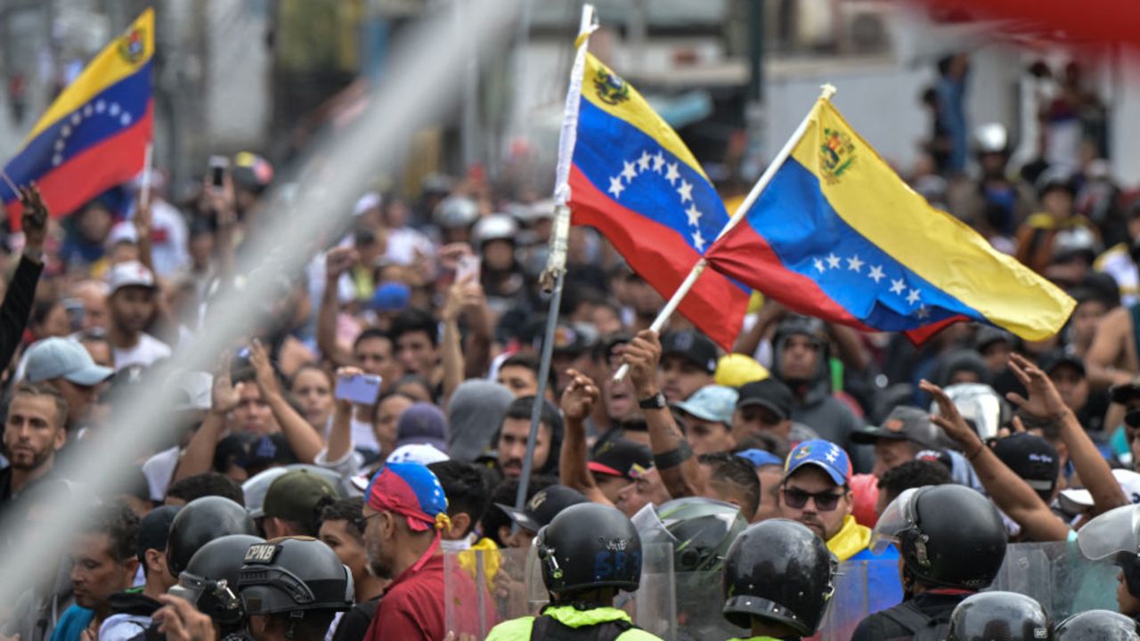 Police officers stand guard next to demonstrators waving Venezuelan flags during a protest against Venezuelan President Nicolas Maduro's government in Caracas on July 29, 2024, a day after the Venezuelan presidential election. Protests erupted in parts of Caracas Monday against the re-election victory claimed by Venezuelan President Nicolas Maduro but disputed by the opposition and questioned internationally, AFP journalists observed. (Photo by Yuri CORTEZ / AFP) (Photo by YURI CORTEZ/AFP via Getty Images)