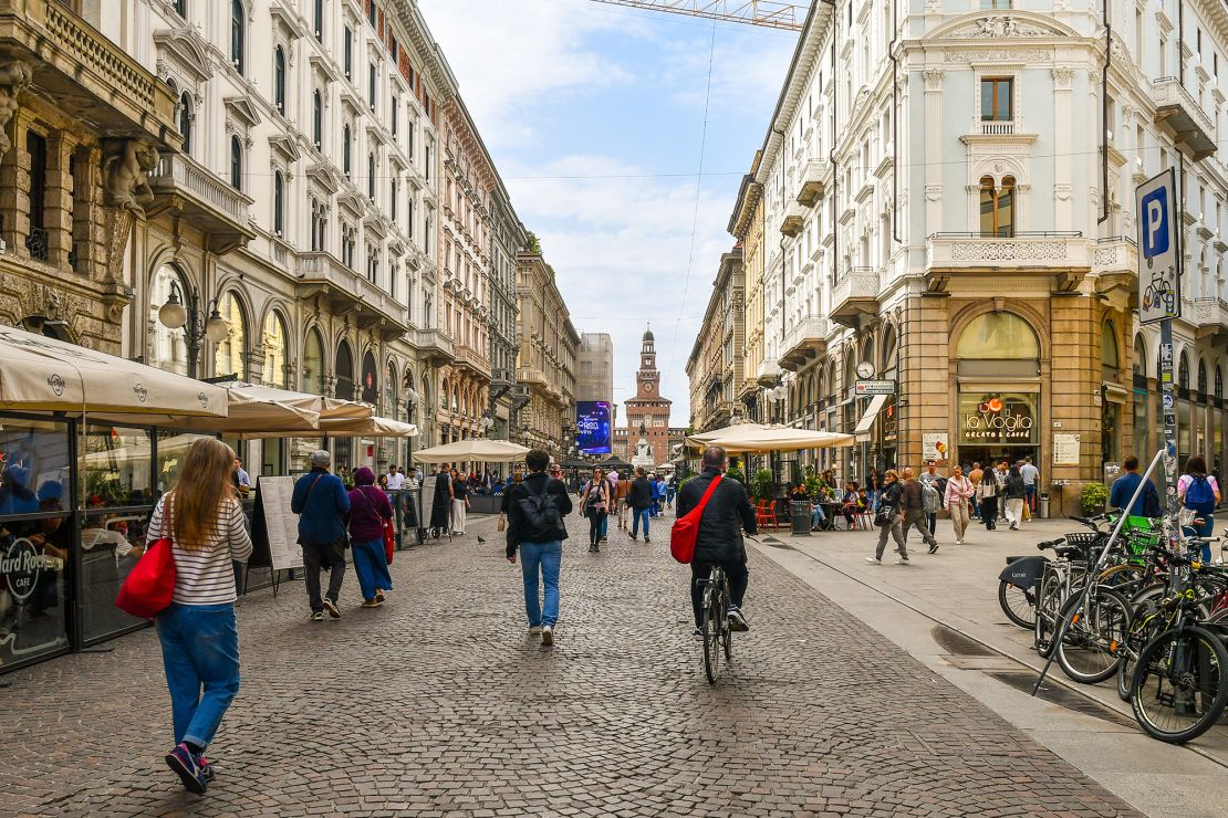 Milan, Lombardy, Italy - 04 29 2024: People walking and cycling in the central Via Dante with the entrance tower of the Castello Sforzesco in the background.