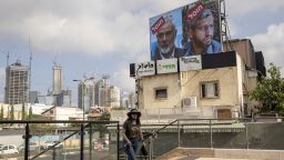 A woman walks near a billboard displaying portraits of Hamas leader Mohammed Deif (R) and Ismail Haniyeh with the slogan "assassinated" reading in Hebrew, in Tel Aviv, on August 2, 2024.