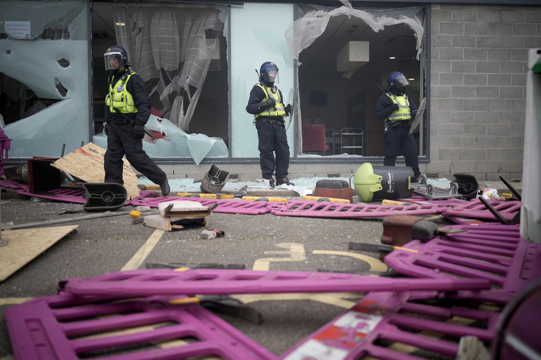 Riot police stand in front of windows broken by rioters outside of the Holiday Inn Express Hotel.