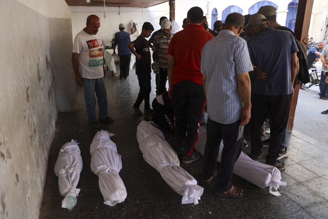 People stand over the shrouded bodies of those killed during Israeli bombardment on the Hassan Salameh and Al-Nassr schools housing displaced Palestinians on August 4, 2024, at the Al-Ahli Arab hospital.