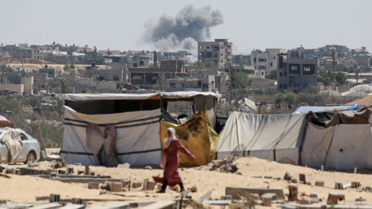 TOPSHOT - Smoke from Israeli bombardment billows in the background as a woman walks in Khan Yunis in the southern Gaza Strip on August 5, 2024, amid the ongoing conflict between Israel and the Palestinian Hamas militant group. (Photo by Bashar TALEB / AFP) (Photo by BASHAR TALEB/AFP via Getty Images)