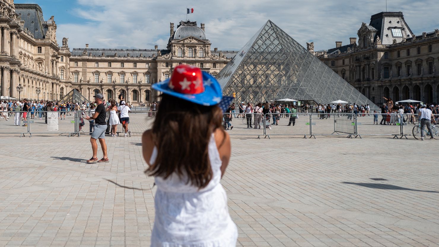 An American tourist wearing a hat in the colors of the American flag looks up at the Louvre pyramid, in Paris, France, on 28 July.