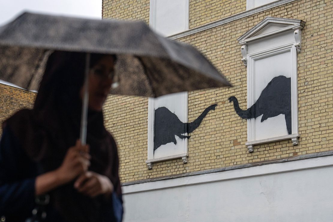 A woman walks past an artwork featuring two elephants by Banksy, spotted on a residential building  August 6, 2024, in London's Chelsea neighborhood.