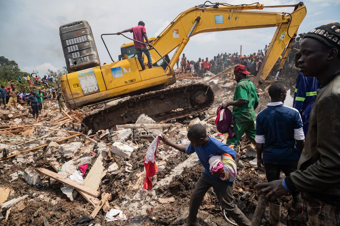 People look on as an excavator helps search for people trapped under debris after a landfill collapsed in Kampala on August 10, 2024.