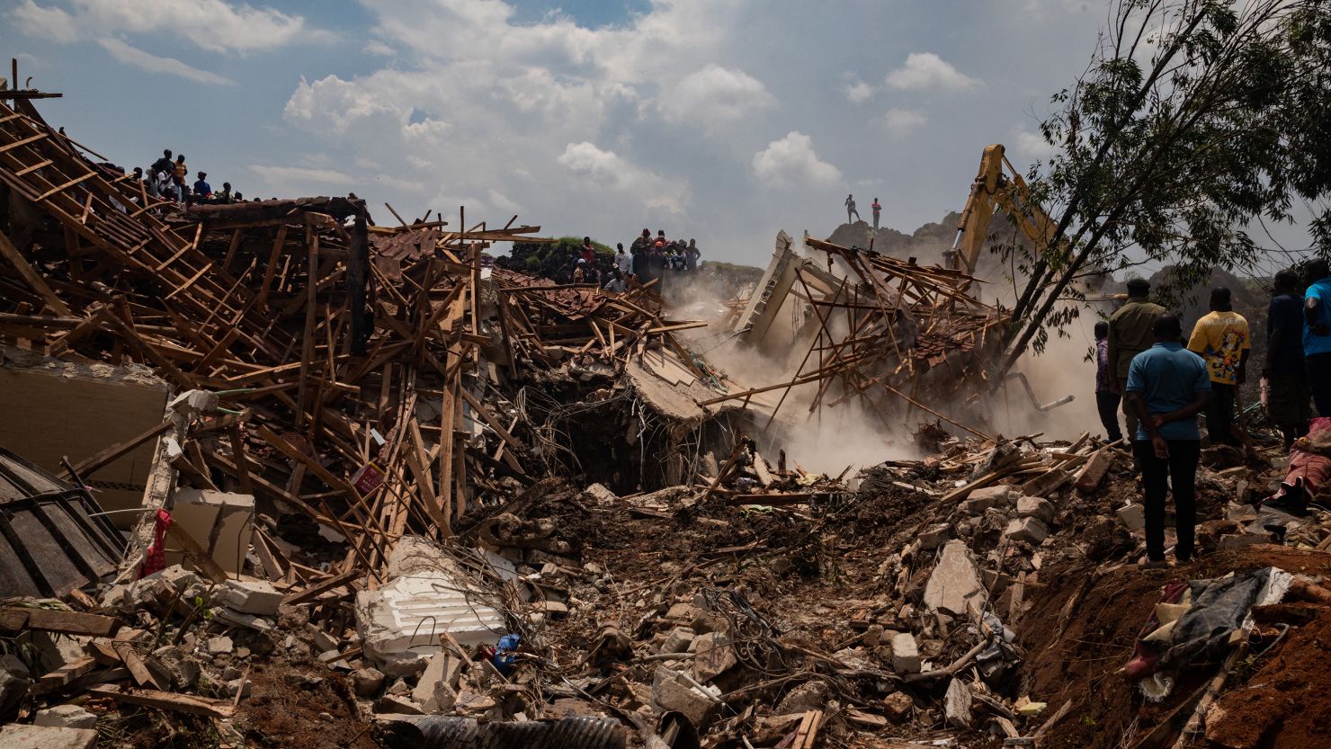 People look on as an excavator helps search for people trapped under debris after a landfill collapsed in Kampala on August 10, 2024.