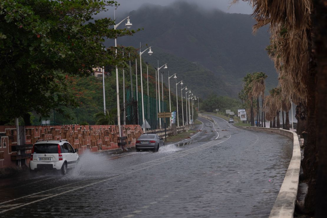 火曜日、フランス領カリブ海島のグアドループのバステル村で、大雨により浸水した道路に沿って自動車が走っている。