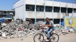 A man cycles past trash and rubble outside a school run by the UN Relief and Works Agency for Palestine Refugees (UNRWA) being used as a makeshift shelter for Palestinians displaced by conflict in the Jabalia camp for Palestinian refugees in the northern Gaza Strip on August 14, 2024 amid the ongoing conflict in the Palestinian territory between Israel and Hamas. (Photo by Omar AL-QATTAA / AFP) (Photo by OMAR AL-QATTAA/AFP via Getty Images)