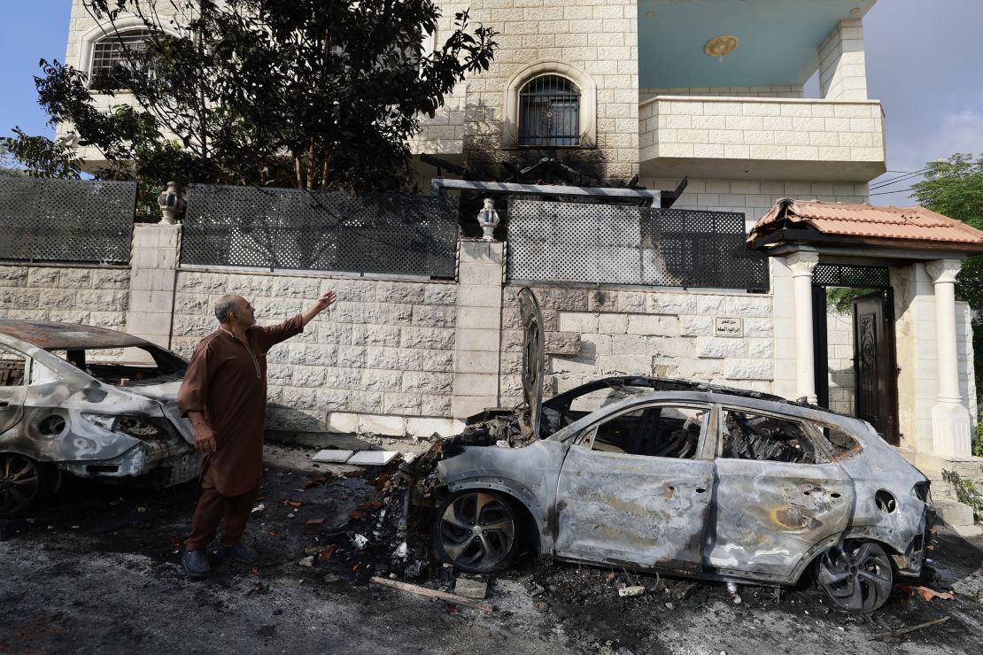 A man standing next to burnt cars points at the damage in his house, a day after an attack by Jewish settlers on the village of Jit near Nablus in the occupied West Bank that left a 23-year-old man dead and others with critical gunshot wounds, on August 16, 2024. Negotiators trying to hash out a Gaza ceasefire deal were due to meet for a second day in Qatar on August 16, after the deadly Jewish settler attack on the Palestinian village drew widespread rebuke, including from Israeli officials. (Photo by Jaafar ASHTIYEH / AFP) (Photo by JAAFAR ASHTIYEH/AFP via Getty Images)