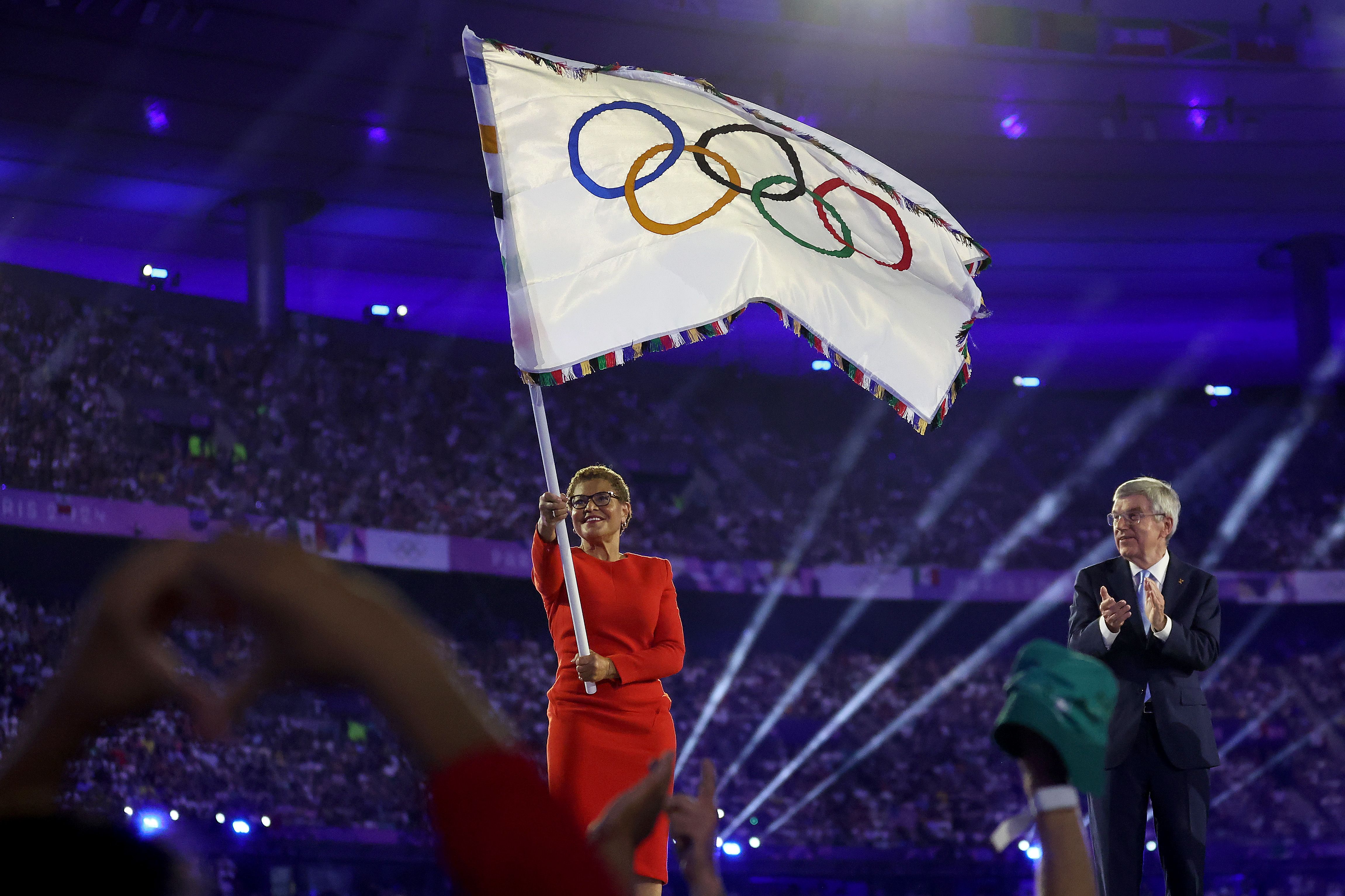 Los Angeles Mayor Karen Bass waves the Olympic flag next to Thomas Bach, the president of the International Olympic Committee.