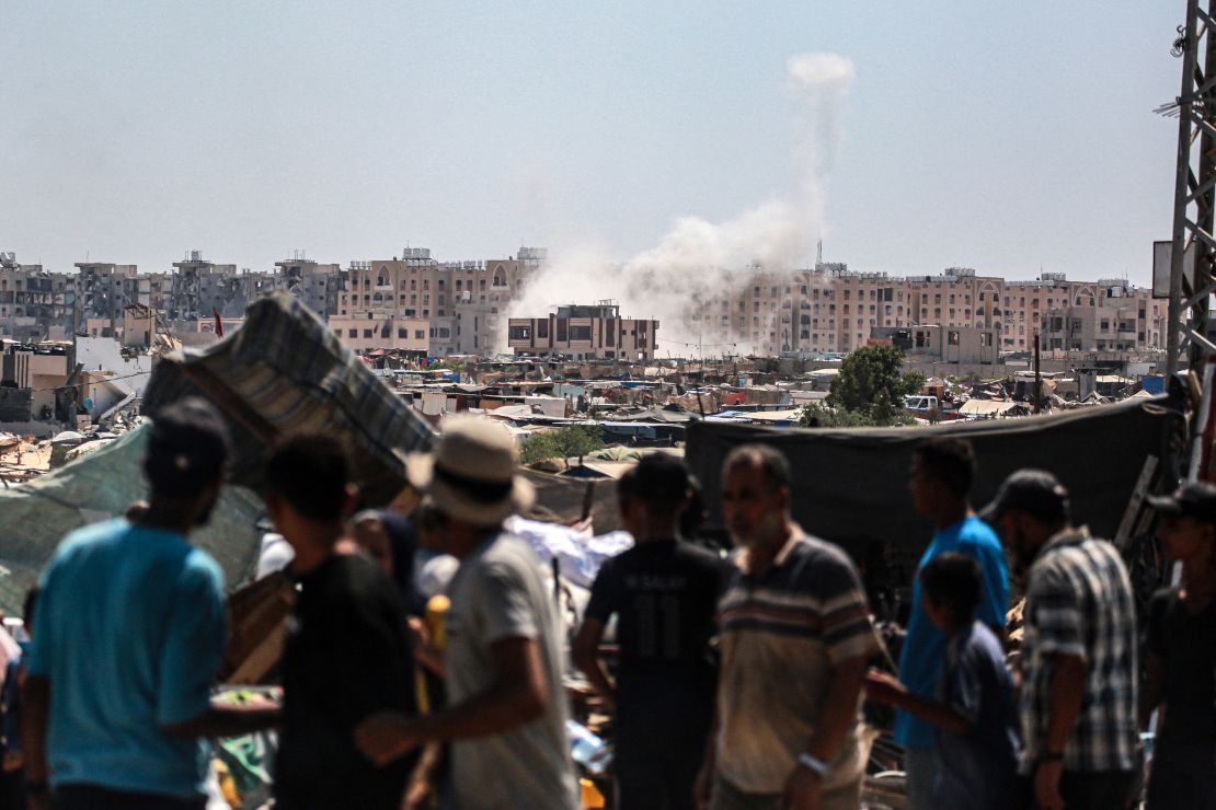 Displaced Palestinians watch from a makeshift camp as shells fired from Israeli tanks hit an area near the Hamad residential complex in Khan Younis in southern Gaza on August 18, 2024.