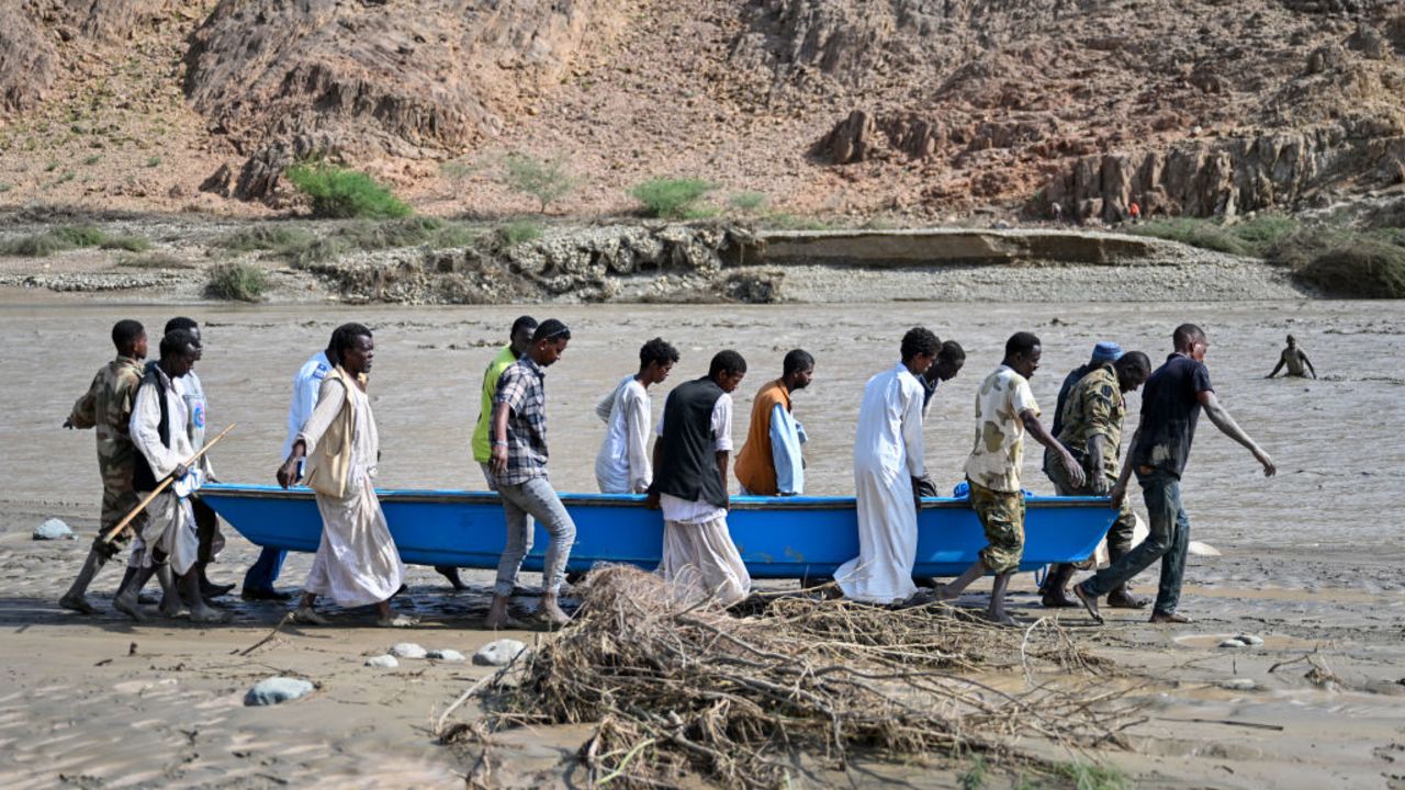 People carry a boat in muddy waters after the collapse of the Arbaat Dam, 40km north of Port Sudan following heavy rains and torrential floods on August 25, 2024. (Photo by AFP) (Photo by -/AFP via Getty Images)