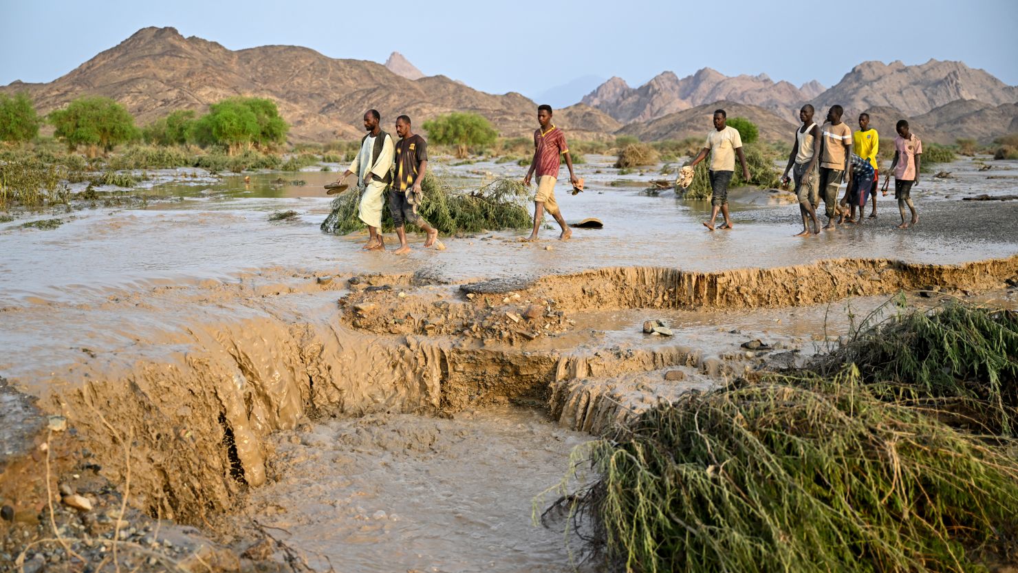 Sudanese people cross a damaged road after the collapse of the Arba'at Dam following heavy rains and torrential floods on August 25, 2024.