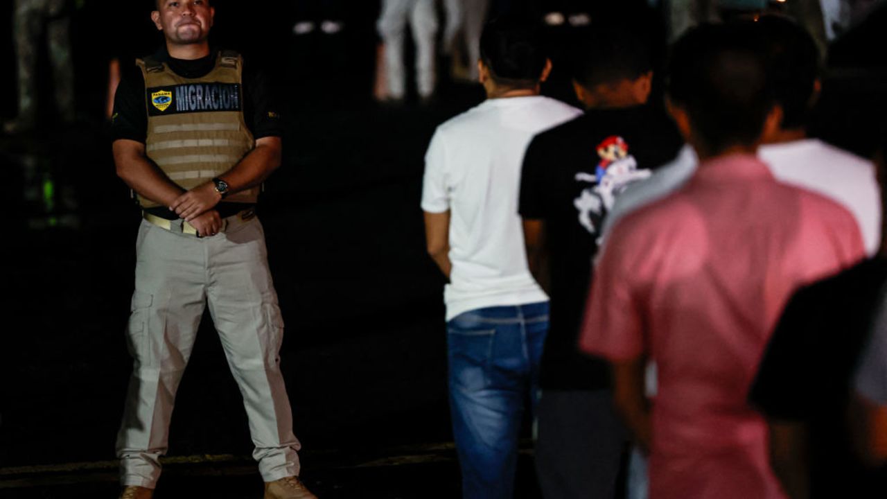 A member of the National Migration Service (SNM) observes Ecuadorian migrants, with their hands and feet handcuffed, queuing to climb a plane at the Albrook Gelabert airport in Panama City on August 29, 2024, during their deportation. Panama on Thursday deported 30 Ecuadorian migrants who entered the country through the inhospitable Darien jungle, bordering Colombia, as part of an agreement signed in July with the United States. (Photo by MARTIN BERNETTI / AFP) (Photo by MARTIN BERNETTI/AFP via Getty Images)