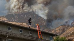 A man waters the roof of his home to protect the house as the Line Fire burns in the foothills of the San Bernardino Mountains, forcing evacuations for neighborhoods in San Bernardino, California on September 7, 2024.