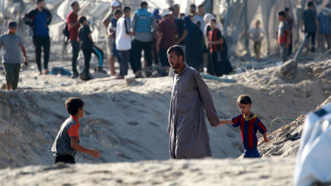 A Palestinian man holds the hand of a child as he and others inspect the damage at the site of Israeli strikes on a makeshift displacement camp in Mawasi Khan Yunis in the Gaza Strip on September 10, 2024, amid the ongoing war between Israel and Palestinian militant group Hamas. Gaza's civil defence agency said that an Israeli strike on a humanitarian zone in the south of the Palestinian territory killed 40 people and wounded 60 others, with the Israeli army saying it had targeted a Hamas command centre in the area. (Photo by Bashar TALEB / AFP) (Photo by BASHAR TALEB/AFP via Getty Images)