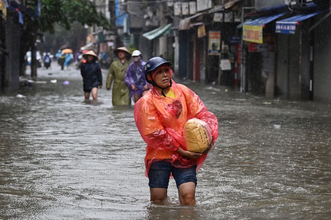 A woman carries a bag of rice through floodwaters on a street in Hanoi on September 11, 2024.