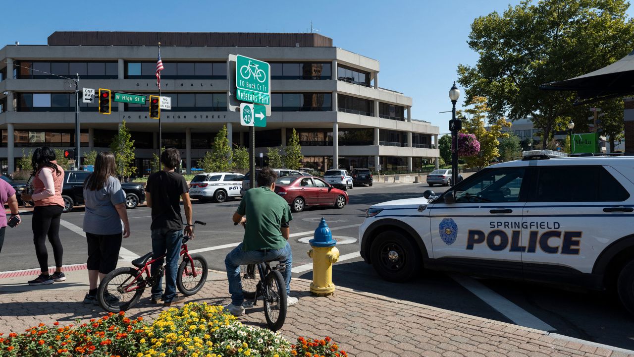 People watch as Springfield Police Department officers investigate the Springfield City Hall after bomb threats were made against buildings earlier in the day in Springfield, Ohio on September 12, 2024. A government building and school were evacuated after an alleged bomb threat Thursday in Springfield, Ohio, local media reported, rattling the small city at the heart of an anti-migrant conspiracy theory amplified by Donald Trump. Springfield has been thrust into the spotlight in recent days after an unfounded story of Haitian migrants eating pets went viral on social media, with the Republican ex-president and current White House candidate pushing the narrative despite it being debunked. (Photo by ROBERTO SCHMIDT / AFP) (Photo by ROBERTO SCHMIDT/AFP via Getty Images)